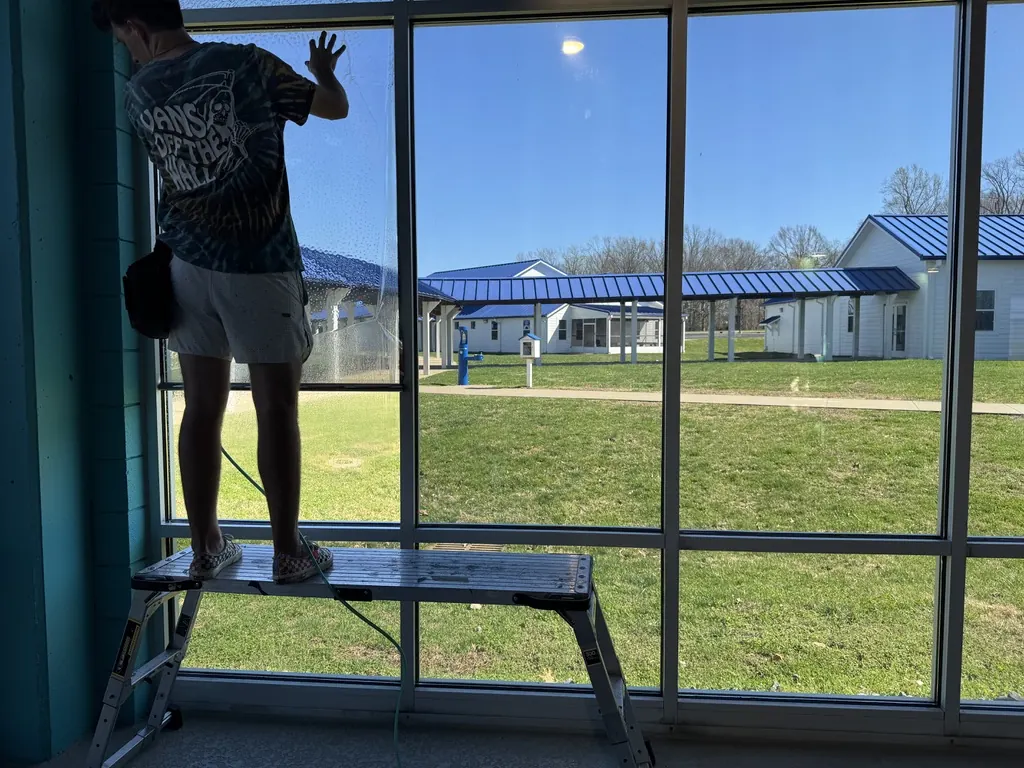 Installer squeegeeing window film on tall glass from a work platform